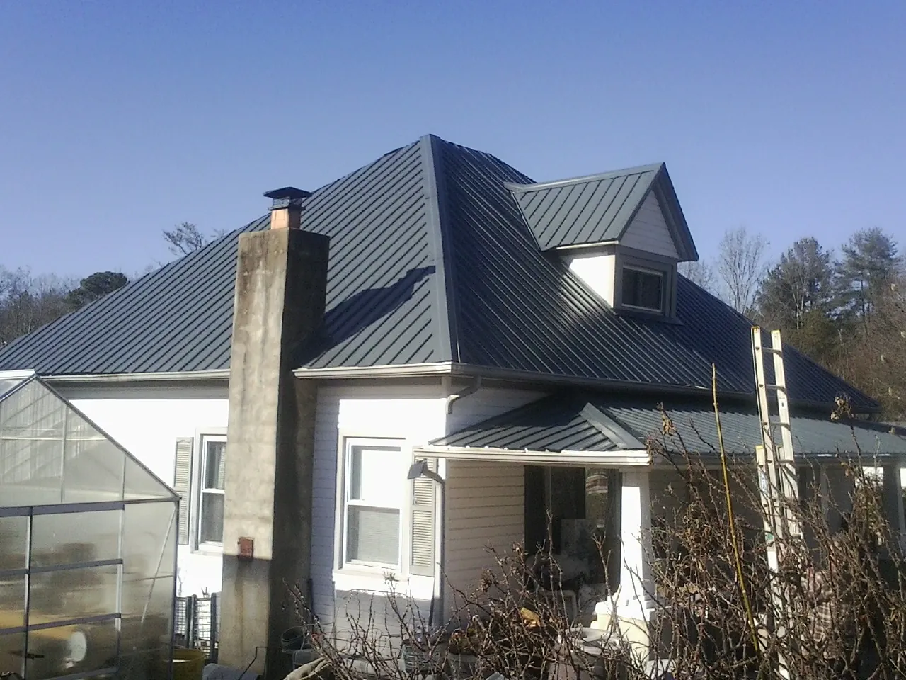 Dark blue standing seam metal roof on a white farmhouse with dormer — Slate & Tile Roof Repair by Roofing Brothers in Fowler
