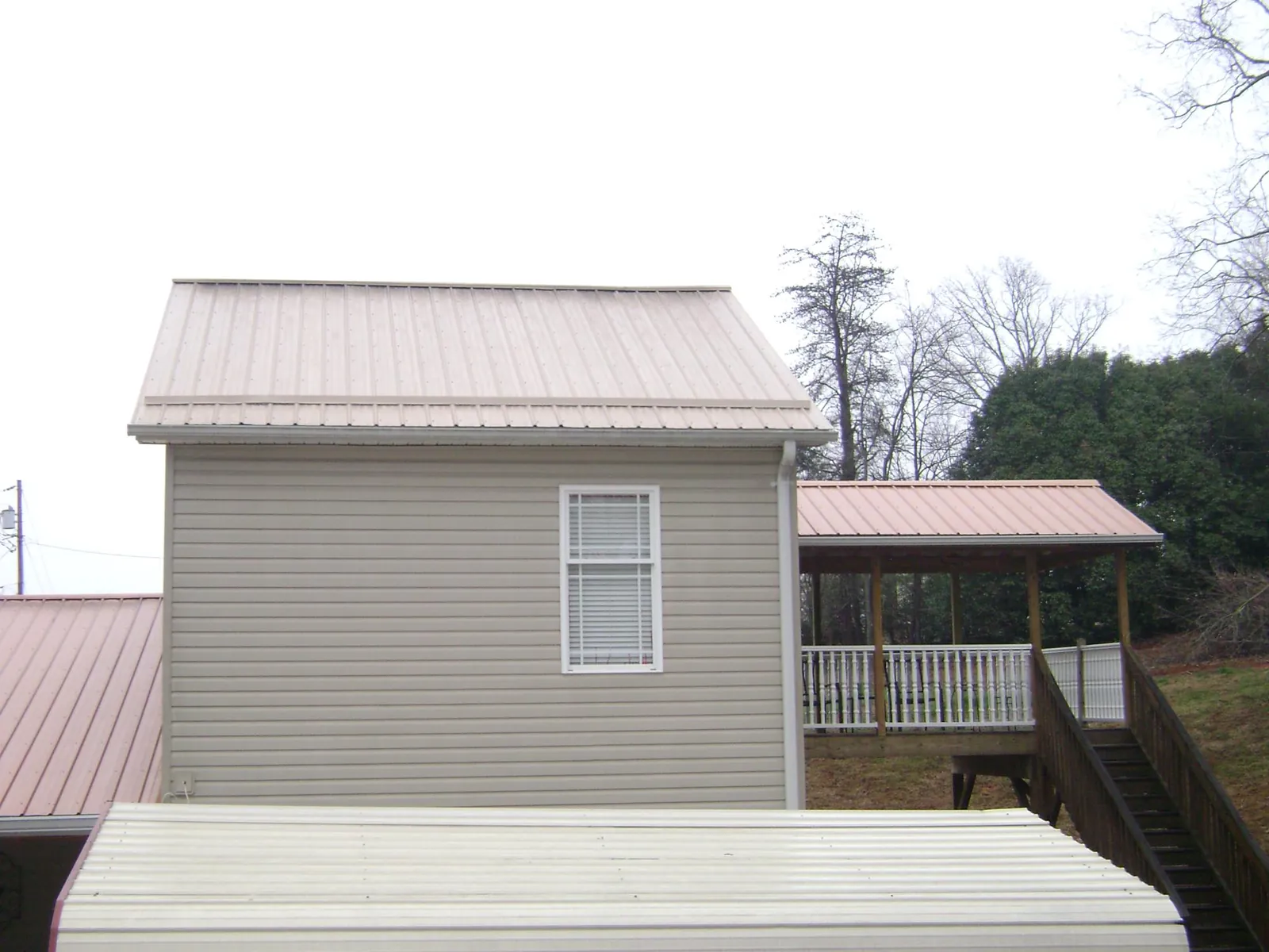 Tan metal roofs on a two story addition and attached porch, from a Roof Replacement job in Fowler